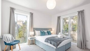 A modern bedroom with a large bed, a chair, and a nightstand. - Lade Braes Apartments (No 22D) (St Andrews)