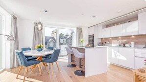 A modern kitchen with white cabinets, a central island, and bar stools. - Lade Braes Apartments (No 22D) (St Andrews)