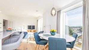A modern dining area with a round table, blue chairs, and a view of the city through large windows. - Lade Braes Apartments (No 22D) (St Andrews)