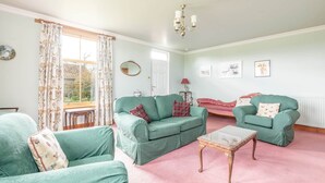 Una sala de estar con dos sofás verdes, una mesita y una ventana con cortinas de flores.