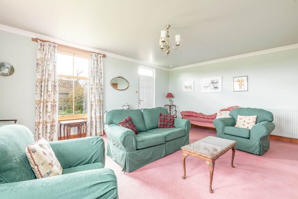 A living room with two green sofas, a small table, and a window with floral curtains.