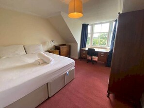 A bedroom with a bed, a desk, a chair, and a window with curtains.
