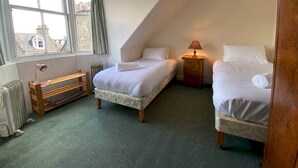 Ein Schlafzimmer mit zwei Betten, einem Fenster mit Vorhängen, einem Heizkörper und einer Lampe auf einem Nachttisch.
