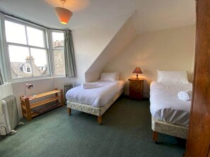 Ein Schlafzimmer mit zwei Betten, einem Fenster, einer Heizung und einer Lampe.
