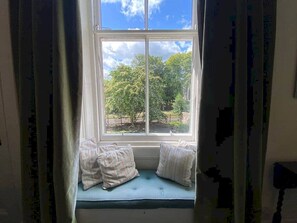 Ein Fenster mit Blick auf einen von Bäumen gesäumten Garten.