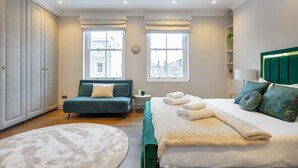 A modern bedroom with a green upholstered sofa, a large bed with white linens, and a round rug. - *| Perfectly Splendid Triplex House in Chelsea |*
 (London)