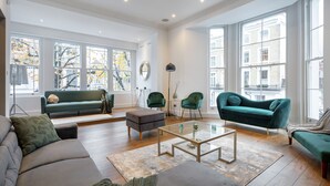 A spacious living room with a large window, a sofa, a coffee table, and two green armchairs. - *| Perfectly Splendid Triplex House in Chelsea |*
 (London)