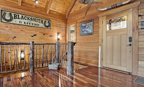 Un intérieur en bois avec une enseigne indiquant « FORGE ET ÉCURIES », une rambarde en bois rustique et une porte dotée d’une fenêtre.