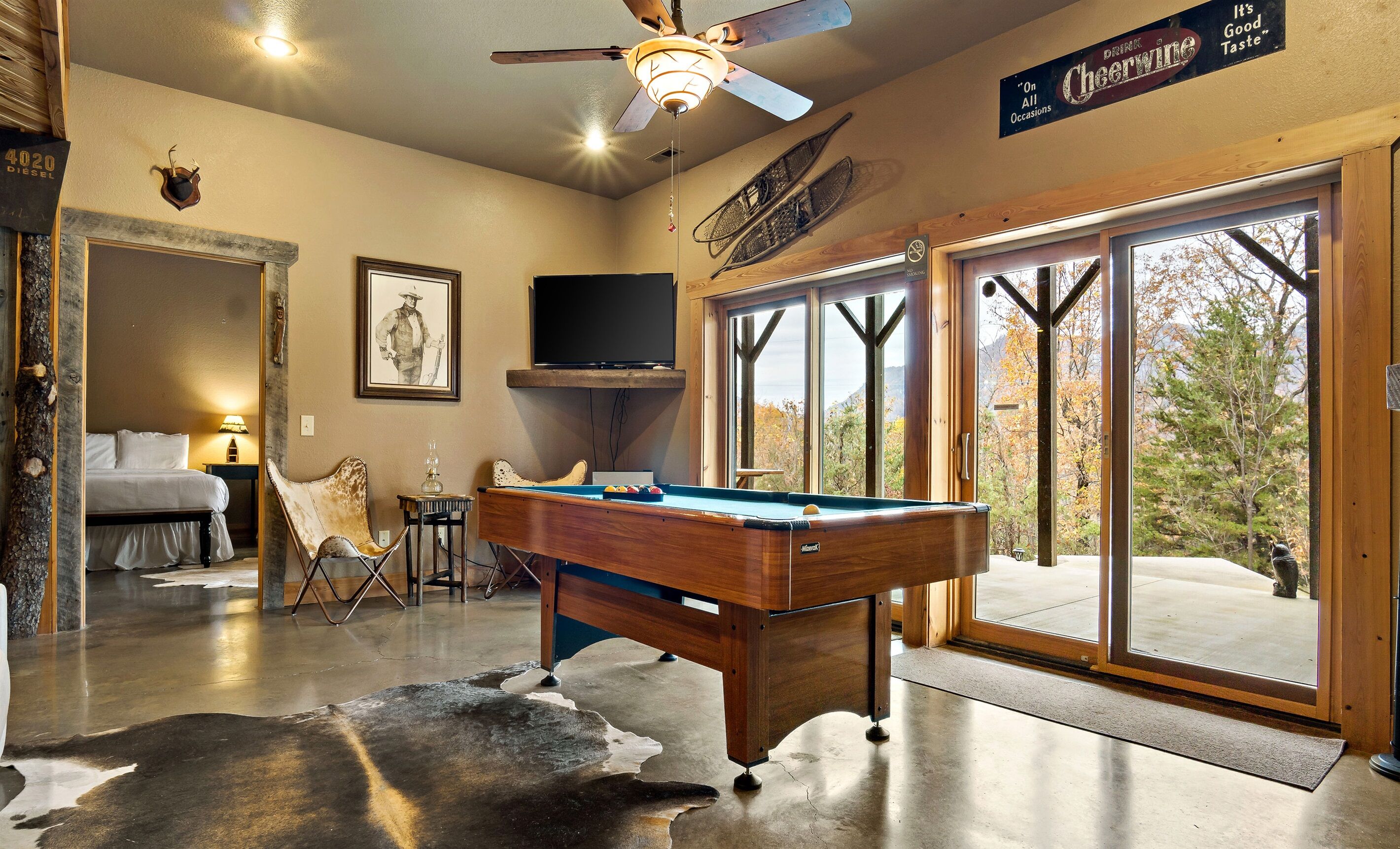 A pool table in a room with a large window, a mounted television, and a ceiling fan.