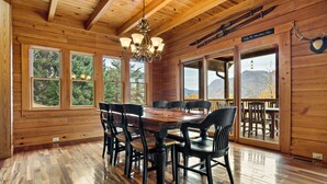 Ein Esszimmer aus Holz mit großem Tisch und Stühlen, großen Fenstern mit Blick auf die Berge und einer Pendelleuchte.