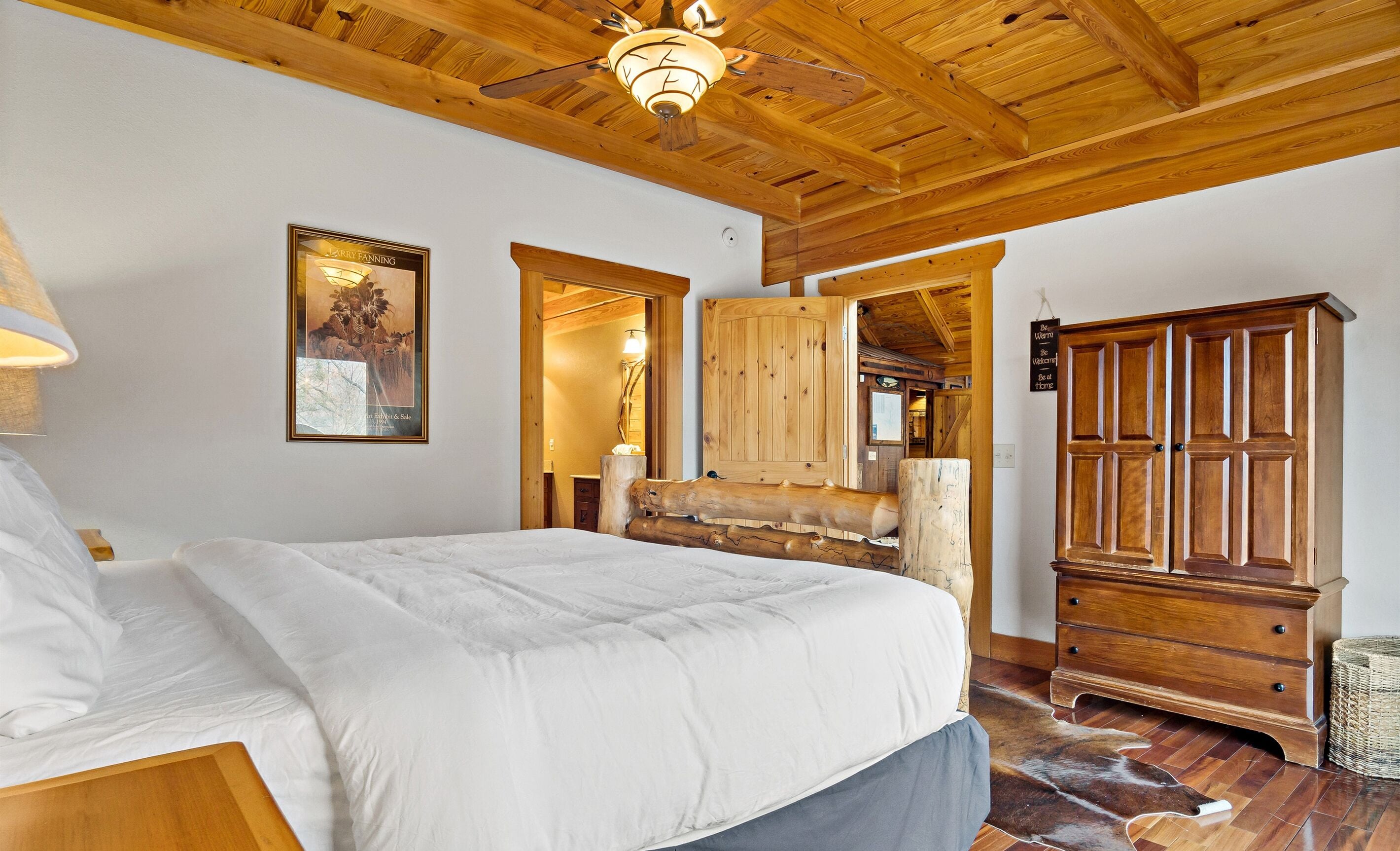 Een slaapkamer met een houten plafond, een groot bed, een houten garderobe en rustieke wanddecoratie.