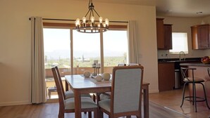 A dining area with a table and chairs, a chandelier, and a view through large windows.