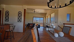 A spacious living area with a wooden bench, a dining table, and a bar area with stools. There are decorative wall sconces and a ceiling fan.