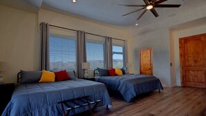 A bedroom with two beds, wooden flooring, a ceiling fan, and a large wooden door.