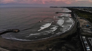 Vista aérea de uma área costeira com praia, estrada e alguns edifícios.