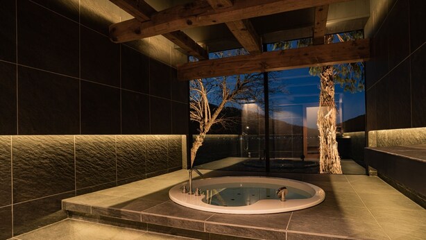 Ein moderner Wellnessbereich mit Whirlpool, Holzbalken und Blick ins Freie im Abenddämmerung.