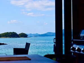Vista de um quarto com mesa e cadeiras, com vista para um corpo d'água calmo, uma ilha distante e montanhas.