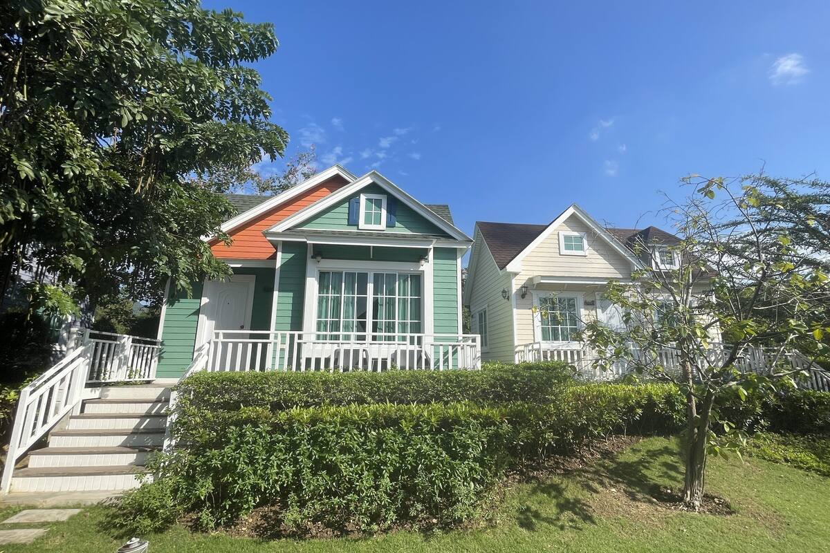 A two-story house with a green and white exterior, a red roof, and a white porch with steps leading to the front door.