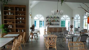 A spacious dining area with high ceilings, large windows, and a variety of seating options including wicker chairs and bar stools. - Vermont Khao Yai (Pak Chong)