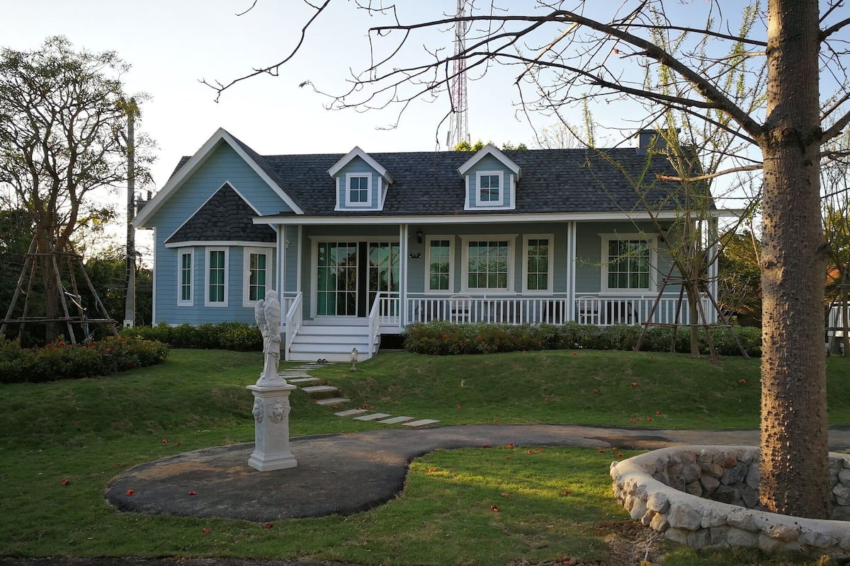 A two-story house with a front porch, a stone pathway, and a statue.