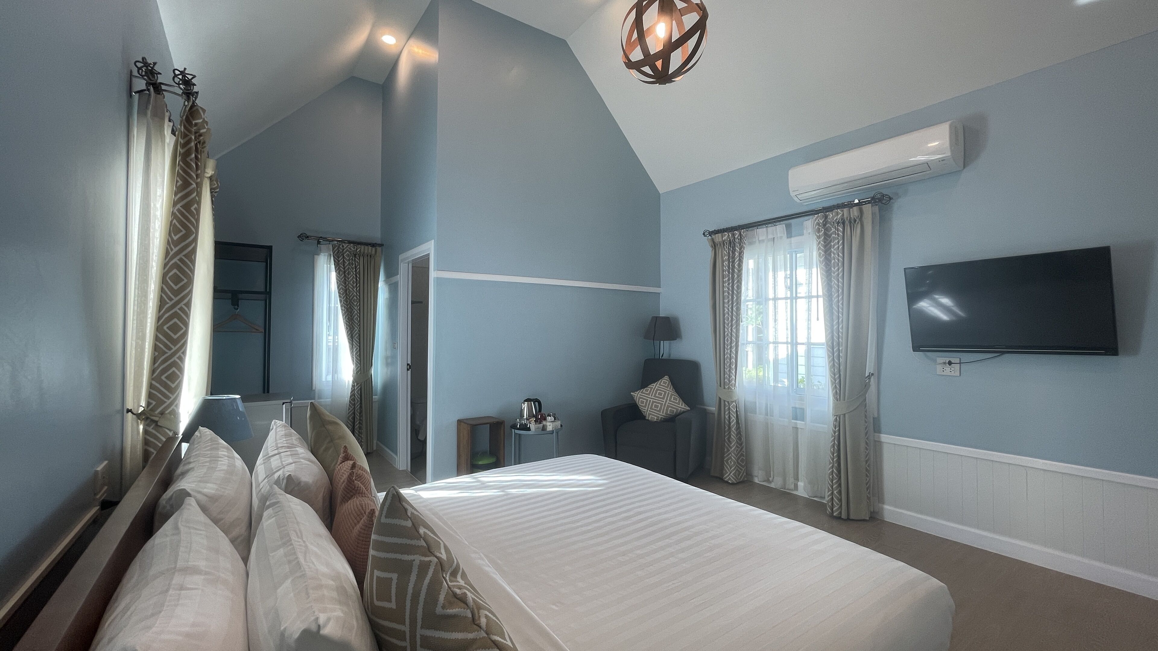 A bedroom with a large bed, a flat-screen TV, a bedside table, and a window with curtains.