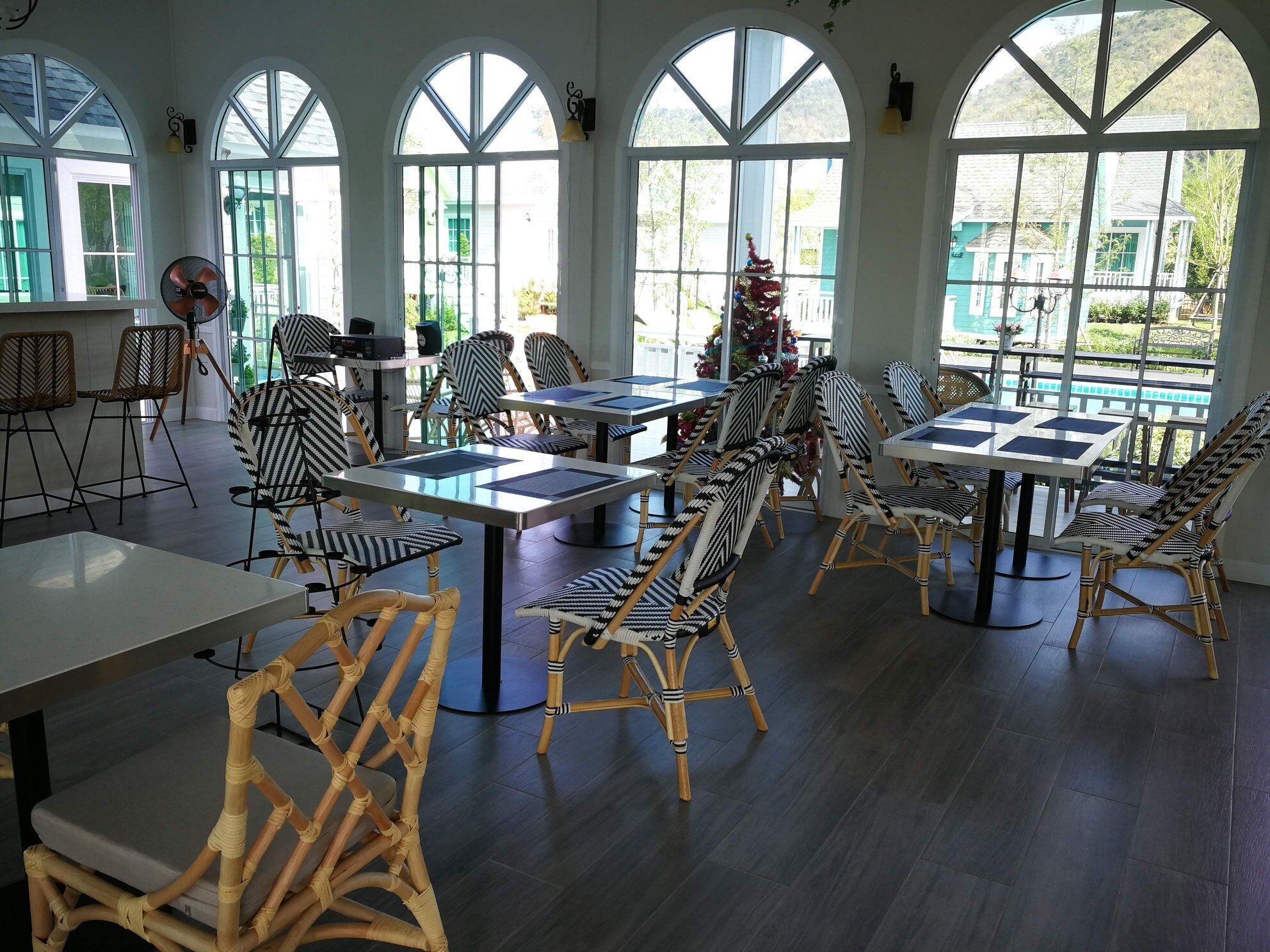 A spacious indoor dining area with high arched windows, wicker chairs, and tables.