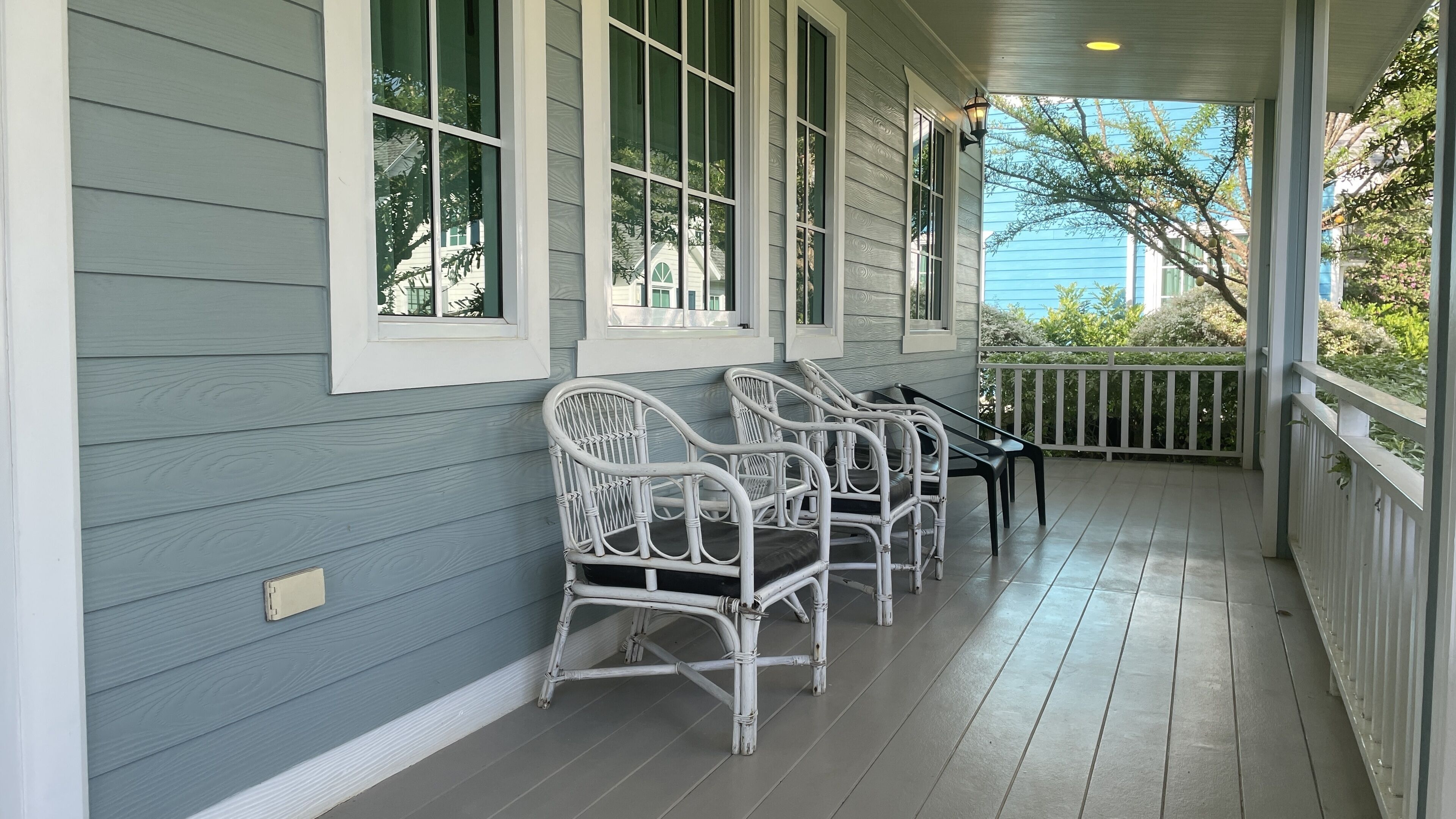 A porch with white wicker chairs and a table, light blue siding, and a white railing.