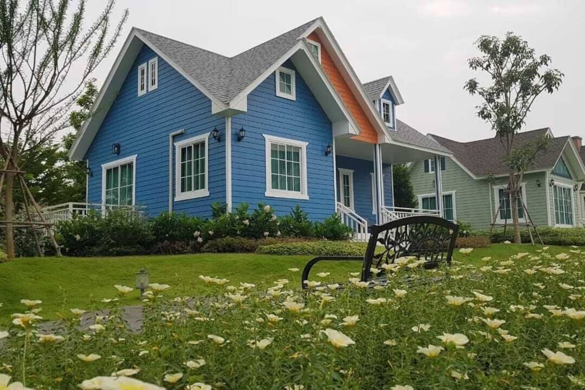 A two-story house with a blue exterior and a green roof, surrounded by a well-maintained lawn and a garden with white flowers.