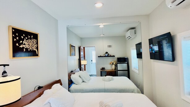 A hotel room with two beds, a desk, a chair, a lamp, an air conditioner, and a TV. - Adorable 1 bedroom mins away to NYC in Teaneck

 (Teaneck)
