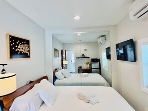 A hotel room with two beds, a desk, a chair, a lamp, an air conditioner, and a TV.