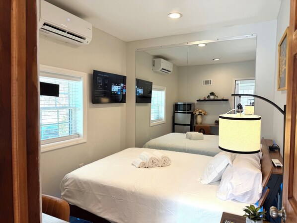 A hotel room with a bed, a desk with a lamp, a mirror, and a TV on the wall.