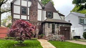 A two-story house with a stone chimney, a small porch, and a well-maintained lawn. - Adorable 1 bedroom mins away to NYC in Teaneck

 (Teaneck)