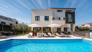 Un bâtiment moderne doté d’une piscine, de chaises longues et de parasols.