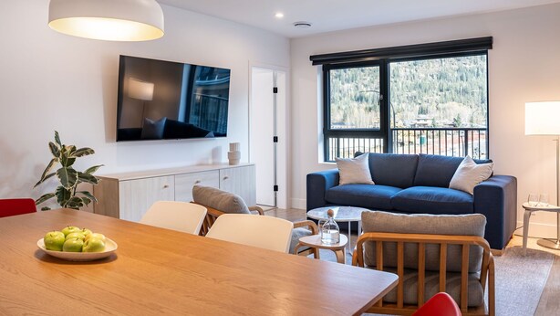 A modern living room with a sofa, dining table, and a TV mounted on the wall. - Hygge Haus By Revelstoke Vacations (Revelstoke)