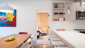 A modern kitchen with white cabinetry, a large island, and a dining area with a wooden table and chairs. - Hygge Haus By Revelstoke Vacations (Revelstoke)