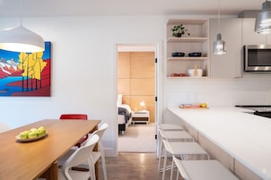 Una cocina moderna con armarios blancos, una isla grande y una zona de comedor con mesa y sillas de madera.