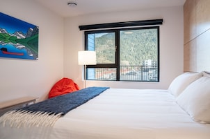 Un cuarto de hotel con una cama grande, una ventana con vista a la montaña, un cuadro en la pared y una silla roja.