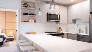 A modern kitchen with white cabinetry, a large island with bar stools, a built-in microwave, and pendant lighting. - Hygge Haus By Revelstoke Vacations (Revelstoke)
