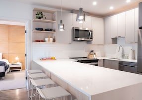 A modern kitchen with white cabinetry, a large island with bar stools, a built-in microwave, and pendant lighting.
