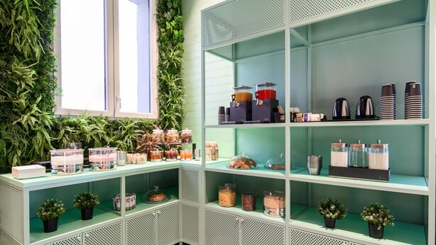 A green metal shelf unit with various food items and containers, a window with a view of greenery, and a small potted plant on the lower shelf. - CX Venice Mestre (Mestre)