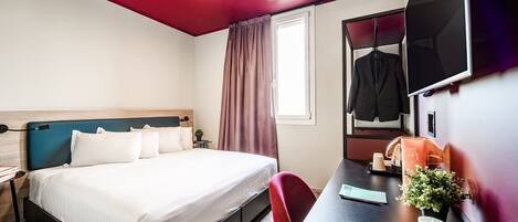 A hotel room with a bed, desk, chair, TV, and a window with curtains.