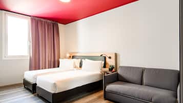 Een hotelkamer met twee bedden, een bank, een nachtkastje en een raam met gordijnen.