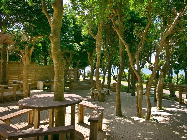 A wooden deck with round tables and benches, surrounded by trees.