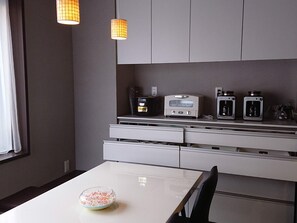 Una cuina moderna amb taulell blanc, microones, cafetera i torradora. Hi ha un bol de cereals sobre la taula.
