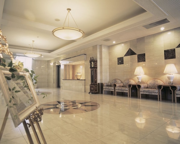 A spacious lobby with a polished floor, a grand clock, and a seating area with lamps.