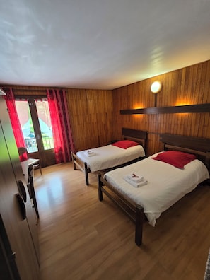 A room with two wooden beds, a wooden wardrobe, and a window with red curtains. - Hôtel et Centre de Montagne Le Choucas (Sixt-Fer-a-Cheval)