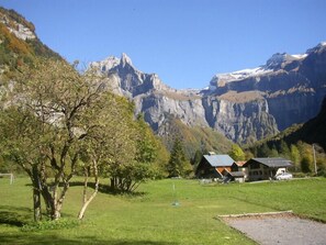 A rural setting with a house surrounded by a green field and mountains in the background. - Hôtel et Centre de Montagne Le Choucas (Sixt-Fer-a-Cheval)