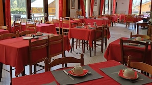 Un restaurante con varias mesas cubiertas de manteles rojos, sillas de madera y vista a un edificio de madera en el exterior.