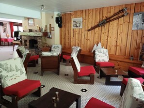 A cozy room with wooden walls, a fireplace, and several chairs with red cushions. - Hôtel et Centre de Montagne Le Choucas (Sixt-Fer-a-Cheval)