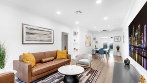 Una sala de estar moderna con un sofá de cuero marrón, una mesa de centro redonda y un mural con vistas a la ciudad en la pared.
